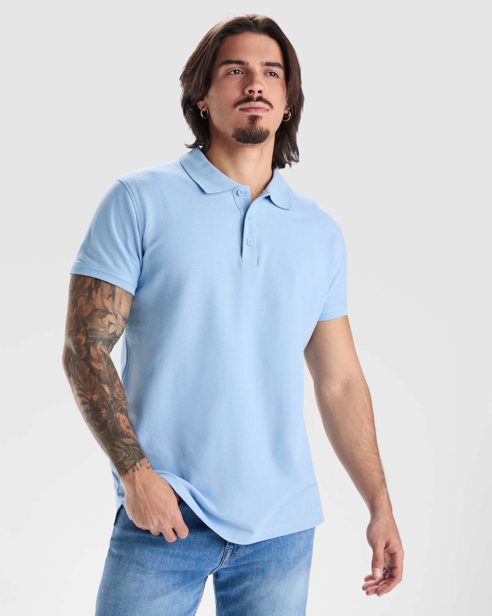 Man wearing a light blue polo shirt and jeans on a plain background